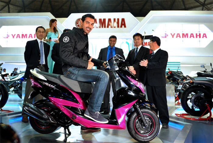 Bollywood actor John Abraham sits on a newly launched scooter as he poses with Yamaha representatives during the 2012 Auto Expo 2012.