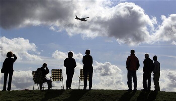 Plane spotters waiting for the first flight of the sixth Boeing 787 test plane look on as a single-engine aircraft flies by. (AP Photo)