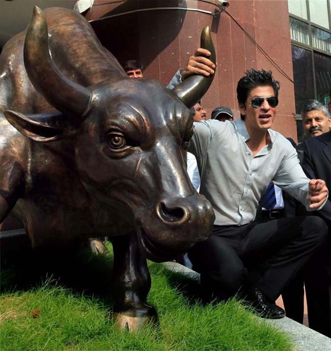 Bollywood actor Shah Rukh Khan poses with the bull-statue at Bombay Stock Exchange during listing of the Eros International Media Limited, in Mumbai on Wednesday. (PTI)