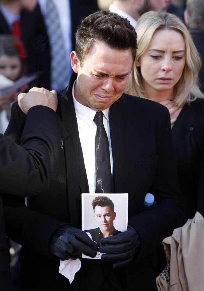 A mourner reacts during the funeral of Stepehn Gately  of Irish band Boyzone, during the funeral service at St. Laurence O'Toole Church, after the funeral service, in Dublin, Ireland, Saturday Oct. 17, 2009. Gately was found dead on Saturday, Oct. 10, 2009, in a house near Port d'Andratx on the western tip of Mallorca. The singer had gone to Mallorca with his partner Andrew Cowles. The two were wed in a civil union in 2006. Autopsy results released on Tuesday showed Gately died of natural causes. Photo of Gately seen on the right. (Photo: AP)