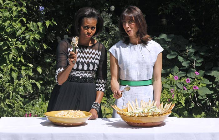 Mrs O chose a crystal embellished black chiffon dress by American designer Tracy Reese as she prepared to serve food with Samantha Cameron, wife of Prime Minister David Cameron, at a barbecue for British and American service members and veterans. Sam Cam opted for an outfit by British designer Jonathan Saunders.