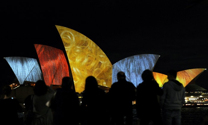 Sydneysiders look on as the Sydney Opera House sails are illuminated by American artist Laurie Anderson for the opening of VIVID Live across Sydney on May 27, 2010. The annual two-week festival of music, film, theatre and visual arts is being curated by Lou Reed and Laurie Anderson and will run until June 11. (Photo: AFP)