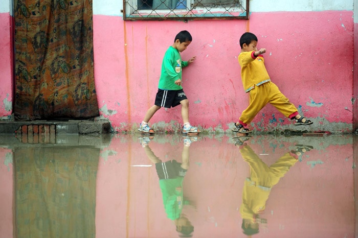 Two Chinese boys step on bricks to avoid the floodwater after a heavy downpour at a school for migrant workers' children in a suburb of Beijing on June 2, 2010. Summer rain storms annually deluge many parts of China, often with devastating results leading to hundreds of fatalities. (Photo: AFP)