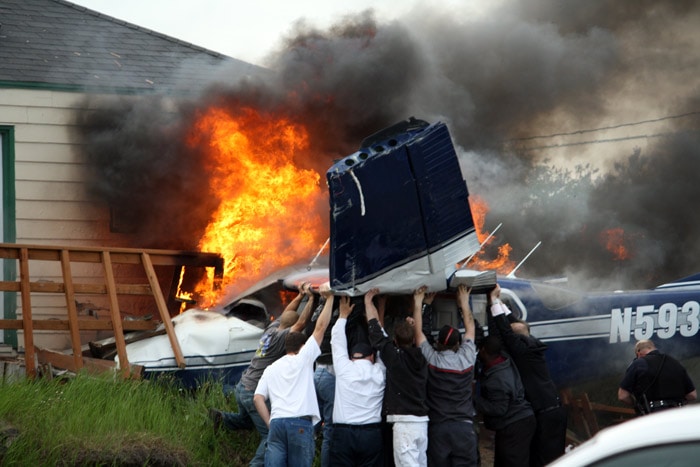 Bystanders try to lift the burning wreckage of a Cessna 206 plane as they search for survivors shortly after it crashed in a busy business district near downtown Anchorage during rush-hour on Tuesday, June 1, 2010. A small child was killed and four other people on board were injured. (Photo: AP)