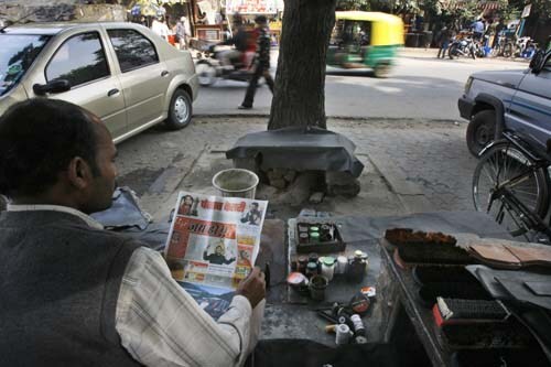 A cobbler reads a local newspaper featuring headlines of <I>Slumdog Millionaire</i>.