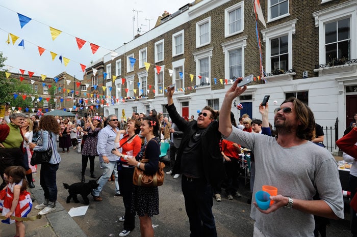 People use their phones to take pictures of a neighbour replicating the Buck palace kiss from their house during a street party.