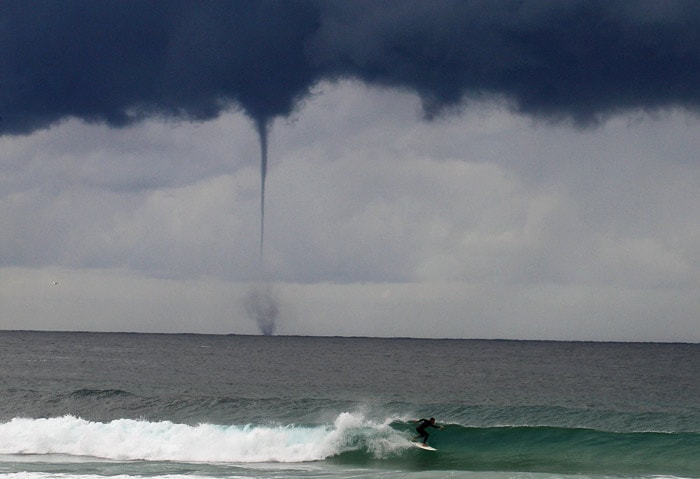 A water spout (tornado) hits the sea behind a surfer on Sydney's Bondi Beach on May 17, 2010. A rare sight in Australia, the water spout lasted around five minutes and expired before landfall. (Photo: AFP)