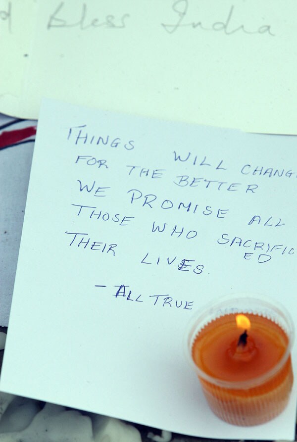 A candle burns over messages placed in front of the Taj hotel in Mumbai on November 30, 2008 while security personnel stand guard as candle-lit memorials were held in front of the Taj hotel by Mumbaikars who came out to mourn the loss of their brothers and sisters.(AFP photo)