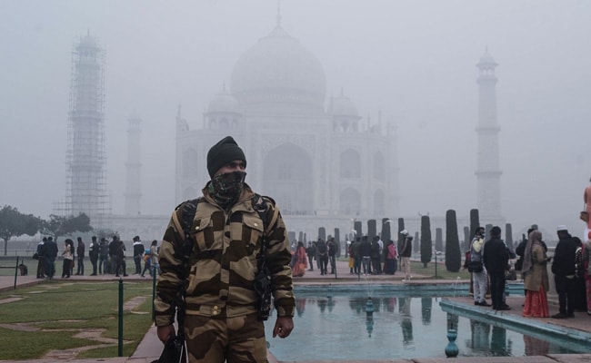 A police personnel stands guard as tourists visit the Taj Mahal in Agra.