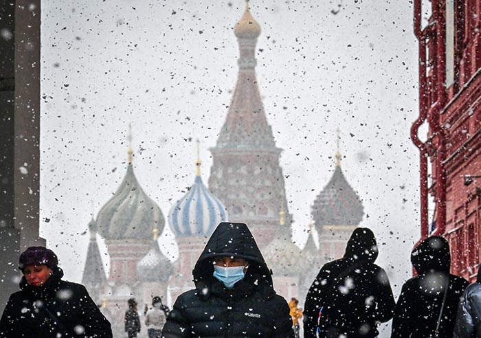 A man wearing a face mask to protect against the Covid-19 disease walks along Red Square with the Saint Basil cathedral during snowfall over Moscow on March 8, 2021.