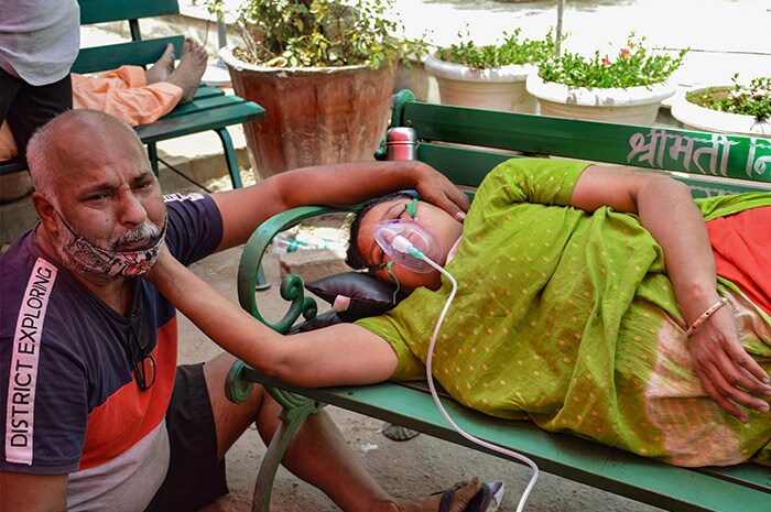 Man sits near his wife a she gets free oxygen, provided by a Sikh organization at Indirapuram Gurdwara for Covid-19 patients, in Ghaziabad.