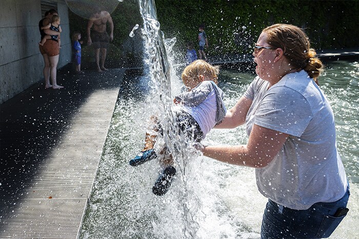 A woman holds a young child under a waterfall at a park in Washington, DC, as a heatwave moves over much of the United States.