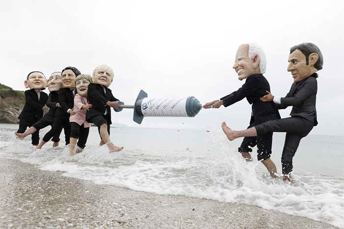 Activists wearing giant heads of the G7 leaders tussle over a COVID-19 vaccine syringe during an action by charity Oxfam to highlight intellectual property for vaccines on Swanpool beach in Falmouth, Cornwall on the sidelines of the G7 summit on June 11, 2021.