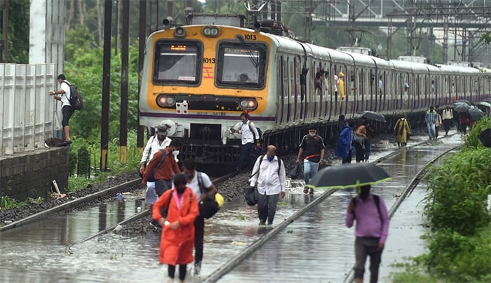 People walk on the waterlogged railway tracks after local trains services were affected due to heavy rain, at Sion in Mumbai, Friday, July 16.