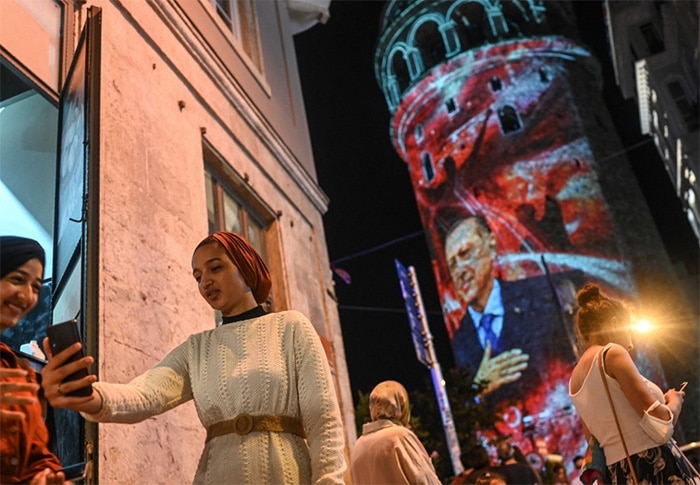 A woman poses for a selfie photograph in front of the Galata tower where is displayed a portrait of Turkish President Recep Tayyip Erdogan, to mark the Democracy and National Unity Day in Istanbul on July 15, 2021.