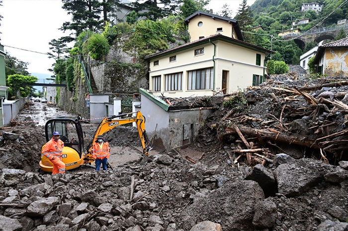 Workers stand by an excavator used to clear the damages caused by a landslide in Laglio after heavy rain caused floods in northern Italy.