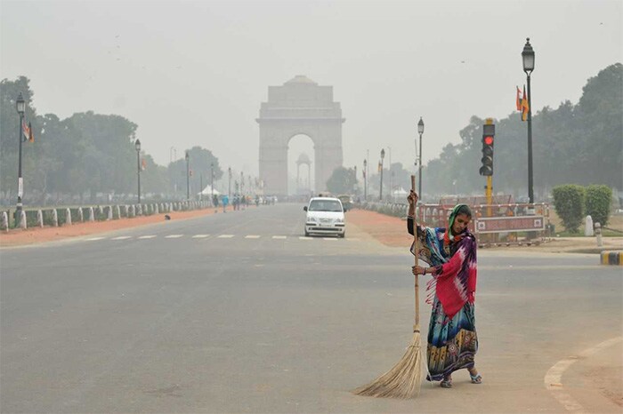 A woman sweeps a road next to India Gate