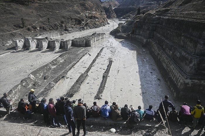 People look at the remains of a dam along a river in Tapovan of Chamoli district.