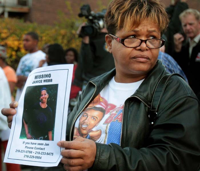 Patricia Warren of Cleveland holds up a poster of her cousin Janice Webb, missing since June of this year, outside the home of Anthony Sowell. The number of bodies found in and near the rapist's home rose to at least 11 when authorities unearthed four corpses from the backyard and found a skull in a bucket in the basement. (AP Photo)