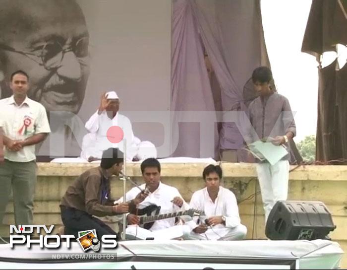 Anna Hazare acknowledges public support, while some of his supporters play music.