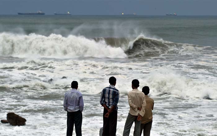 Youths stand on the shore as high tidal waves hit the coastline in Visakhapatnam, Andhra Pradesh.