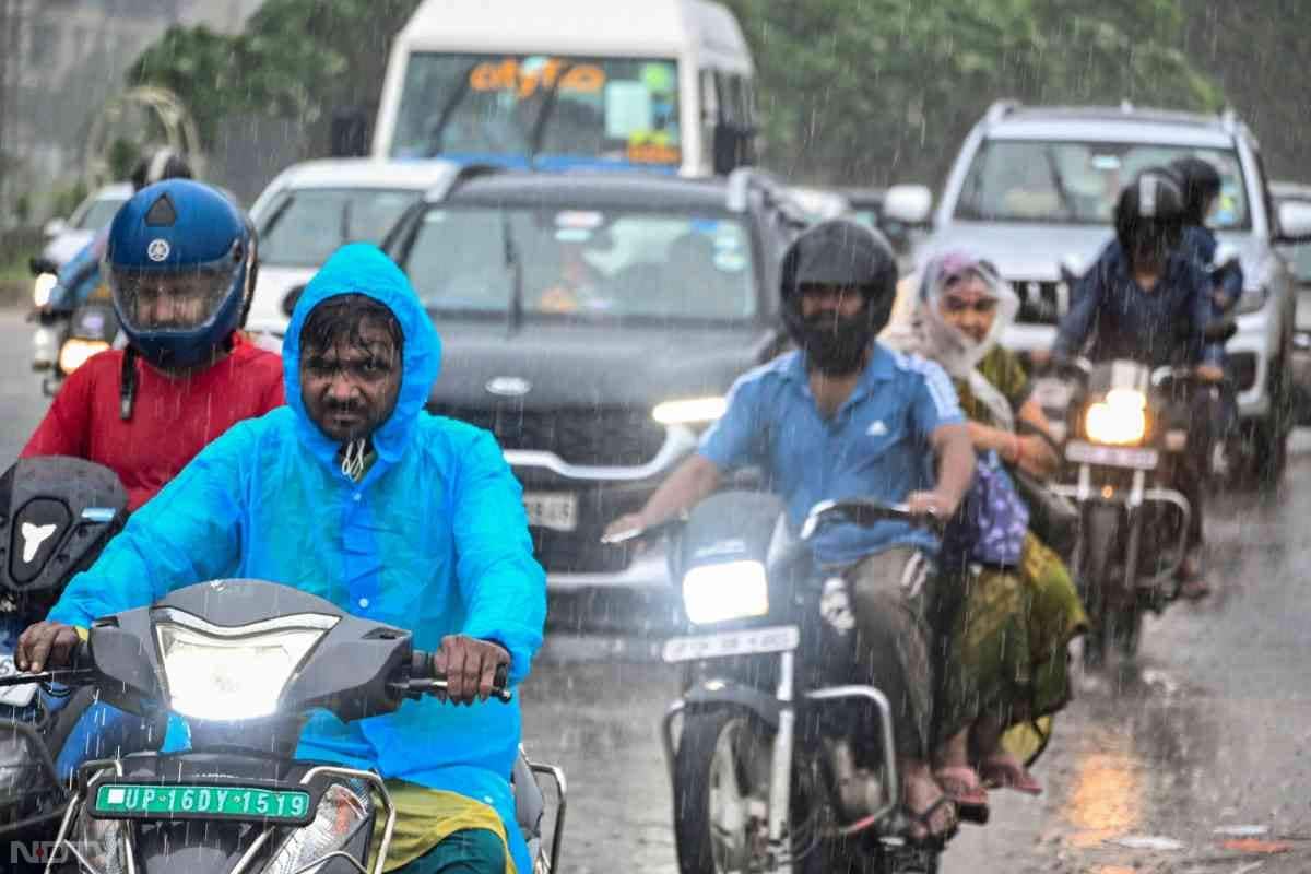 दिल्ली-एनसीआर में भारी बारिश के बीच बाइक सवार लोग रेनकोट पहनकर काम पर निकल पड़े