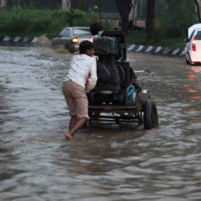 A rickshaw puller pushes his loaded vehicle as vehicles wade through a flooded street after a heavy downpour in New Delhi on Wednesday. (PTI Photo)