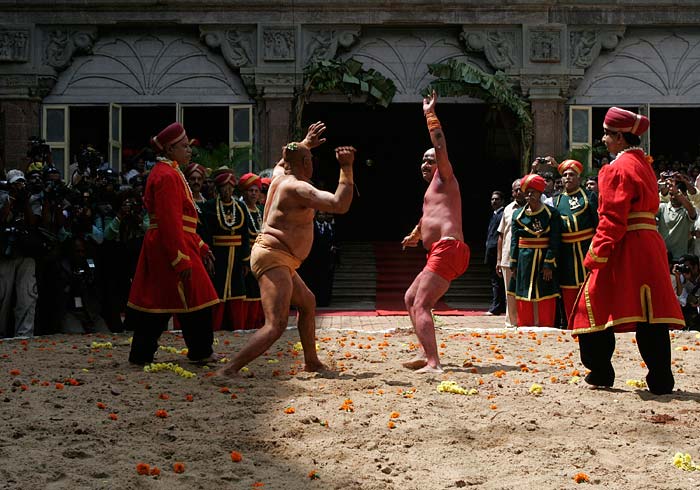 A referee, in red robe, looks on as wrestlers engage in a bout of traditional wrestling as part of celebrations at the Mysore Palace on the last day of Dusshera festival