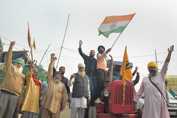 A man waves the national flag atop a tractor amid farmers' celebration over the repeal of the three farm laws, at Ghazipur border.