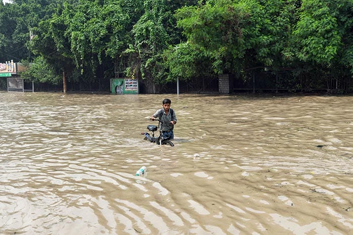 कश्मीरी गेट के पास स्थित निचले इलाकों में भरे पानी में से एक आदमी अपनी साइकिल को धकेलता हुआ नज़र आया. (फोटो: एएनआई)