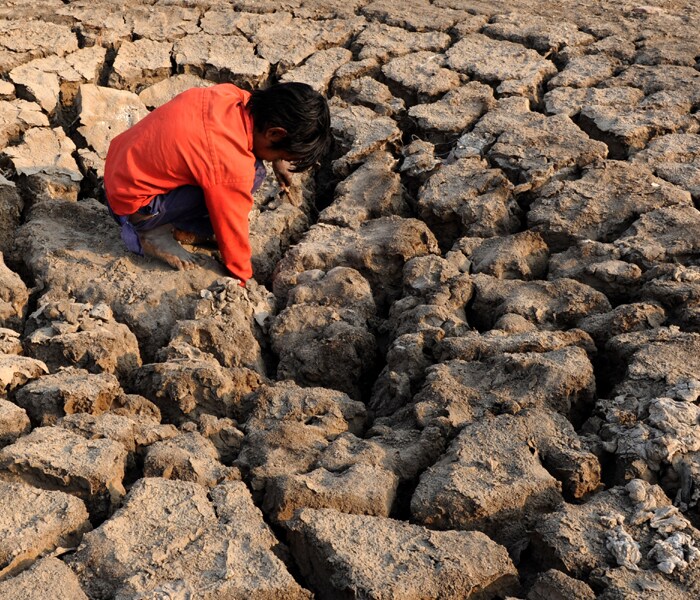 <b>Digging deep:</b>A child tries to figure out the depth of a crack that has developed in a parched field. (AFP image)