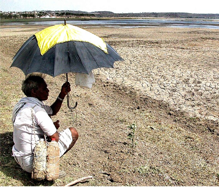 <b>Bought for the rains, used for the sun:</b>A man tries to escape the heat by using an umbrella to cover himself. The scorching sun has offered little respite for him this time around. (AFP image)