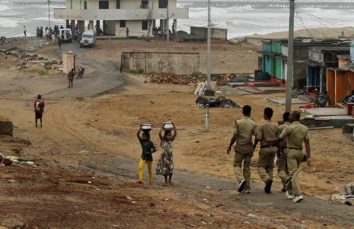 Children walk carrying water as policemen arrive to evacuate people on the Bay of Bengal coast at Gopalpur, Orissa