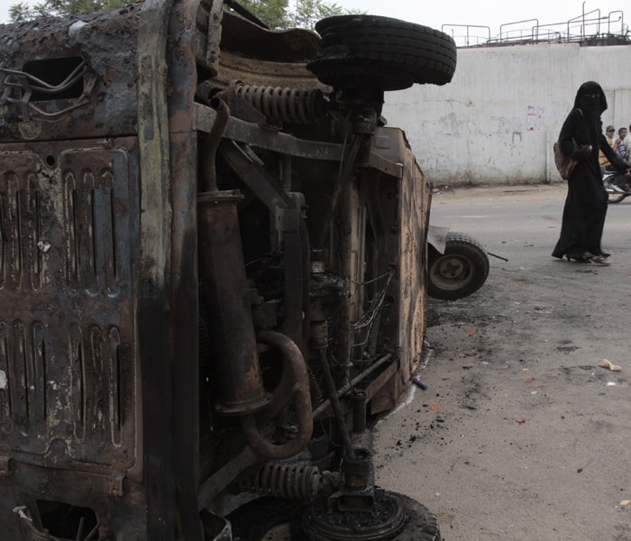 A woman walks past an auto rickshaw that was destroyed in the riots. Authorities fired tear gas and warning shots and swung batons to disperse angry crowd who attacked each other with stones and clubs.(AP photo)