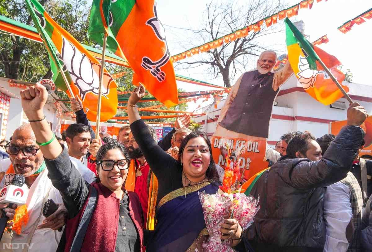 BJP supporters wave party flags as they celebrate the party's massive win in the Delhi Assembly elections.