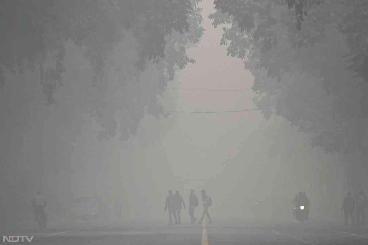 Pedestrians walk across a street on a cold smoggy morning in New Delhi on November 18