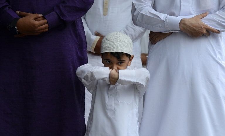 A child looks on as poeople offer Eid prayers on a street in the Masab Tank Area of Hyderabad. (AFP Photo)