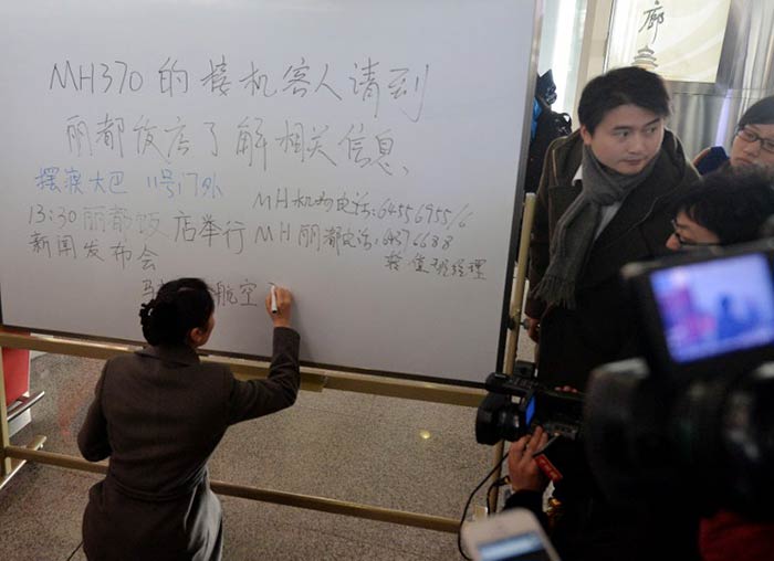 A worker at the Beijing airport writes on a sign board advising relatives of the missing passengers to go to a nearby hotel for information on the flight.