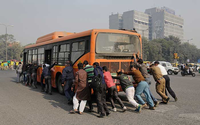 Passengers and traffic policemen push a bus after it broke down at a traffic intersection on the first day of the odd-even campaign.