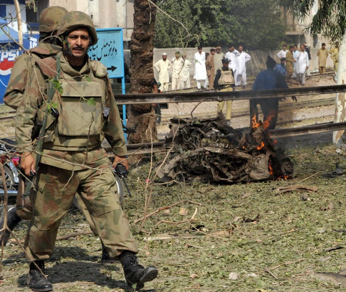 Pakistani soldiers walk beside the burning wreckage of a car used in a suicide bomb blast after an attack on a police building in Peshawar. A suicide car bomber tore through a police building in Pakistan on October 16, killing 11 people and exacerbating public anger over security breaches behind a wave of recent attacks.