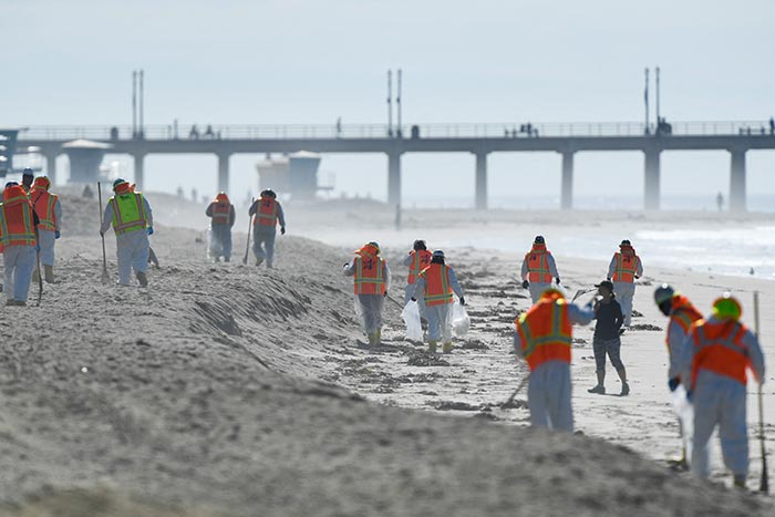 Environmental crews wear PPE as they walk on the beach to clean up debris after an oil spill in the Pacific Ocean in Huntington Beach, California.