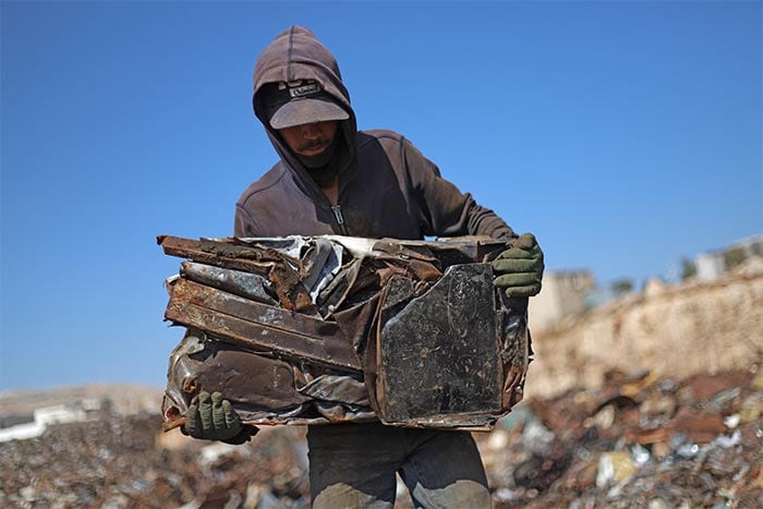 A man walks with a cube of compacted scrap metal at a wrecking yard (junkyard) employing Syrians displaced by conflict.