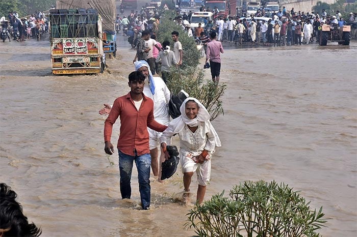 Commuters wade through a flooded national highway after river Kosi overflowed following heavy rains near Rampur in Uttar Pradesh.