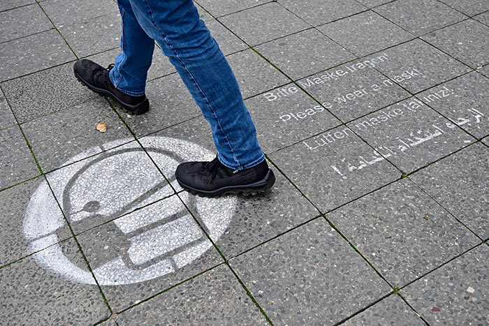 A pedestrian walks along a pavement featuring a public health announcement calling for people to wear face masks during the ongoing Covid-19 pandemic in Berlin.