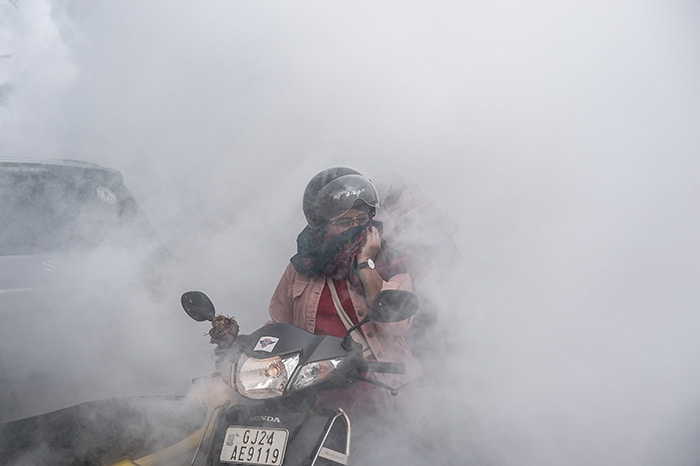 A motorist covers her face as workers fumigate an area as a preventive measure against mosquito-born diseases in Ahmedabad.