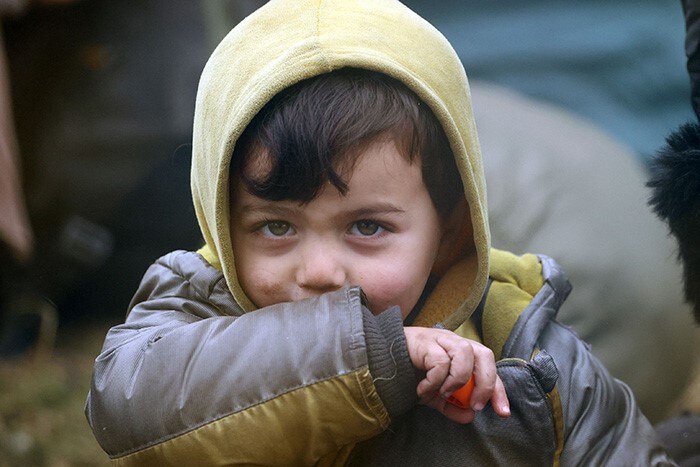 A kid looks into the camera as migrants aiming to cross into Poland camp near the Bruzgi-Kuznica border crossing on the Belarusian-Polish border.