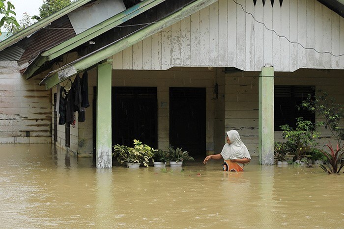 A woman wades in floodwaters outside her home in Matangkuli, Aceh.