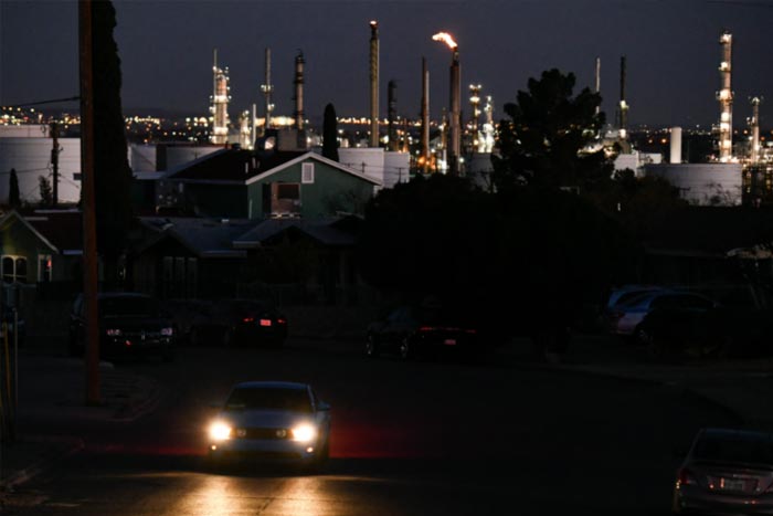 A vehicle drives through a neighborhood as a flaring tower and storage tanks stand on the horizon at the Marathon Petroleum Corp. El Paso oil refinery.