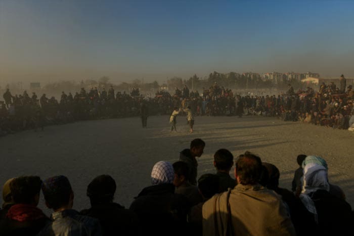 Afghan people watch as wrestlers in the foreground compete in a traditional bout of mud wrestling at a ground in Chaman-e-Hozori area in Kabul.