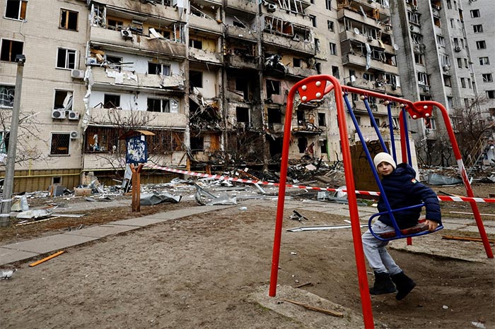 A child sits on a swing in front of a damaged residential building in Kyiv.